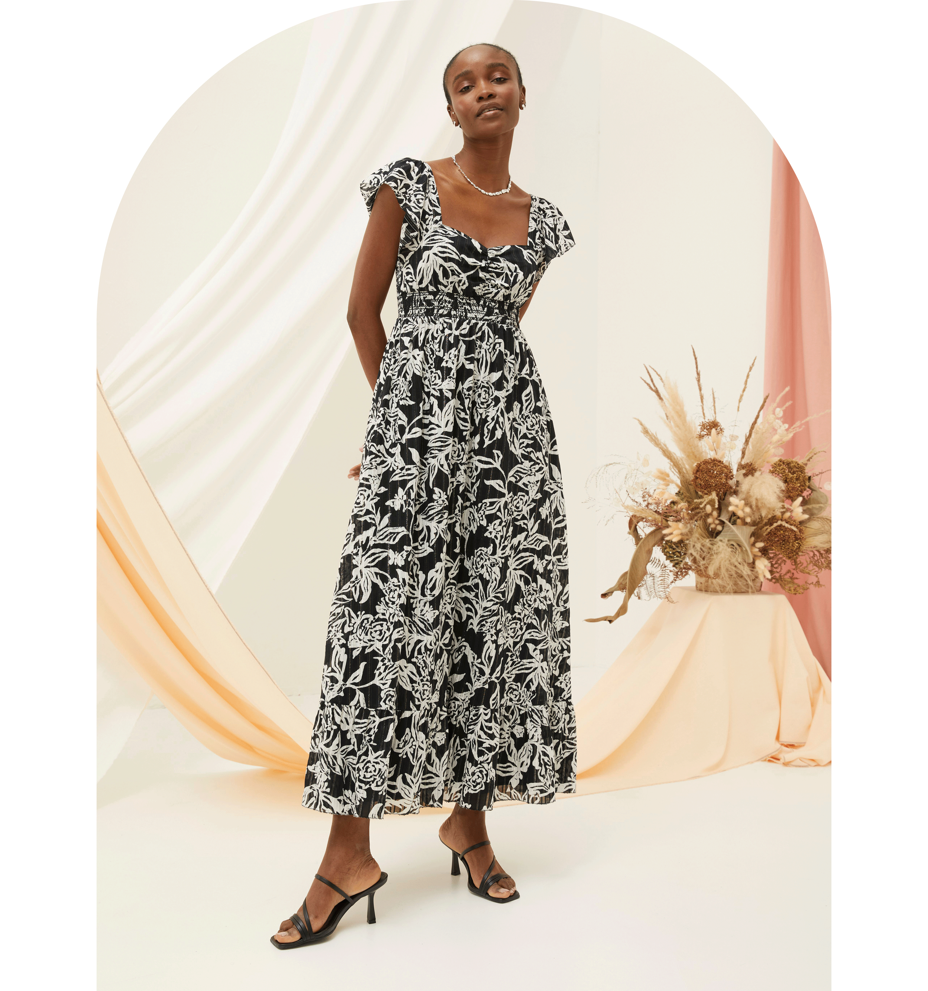 A woman wearing a black & white floral print midi dress with short sleeves, square neckline, shirred waist & side pockets.
